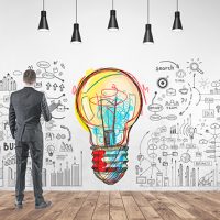 Rear view of a young businessman in a gray suit holding a folder. He is looking forward. A good business idea and a start up mind map on a concrete wall